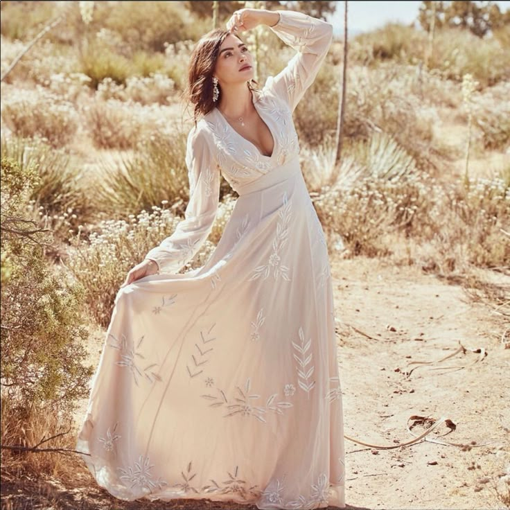 a woman in a long white dress is posing for a photo on the dirt road