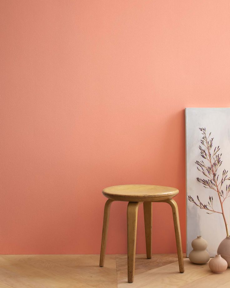 a small wooden stool next to a pink wall and two vases on the floor