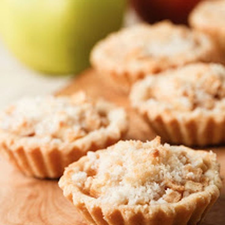 some muffins sitting on top of a wooden cutting board next to an apple