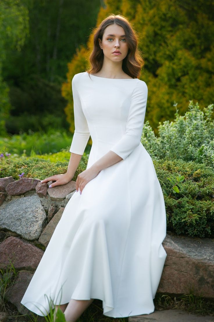 a woman in a white dress is sitting on some rocks and looking at the camera