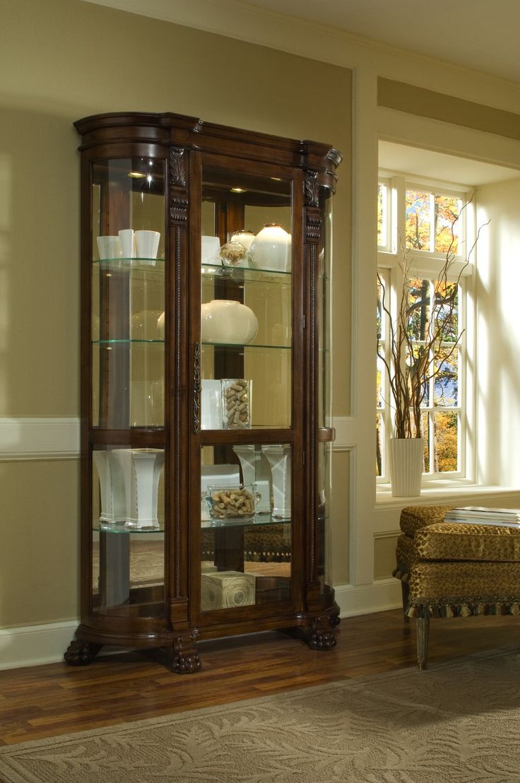 Museum-quality display options are at your fingertips with this well-scaled curved side curio in your home. The back of this tall curio cabinet sits flush against your wall to maximize visual impact without taking up too much floor space. The sides are curved maximizing the view of the mirror-backed interior. The single door opens from the front and is framed with ornate woodwork. Once the door is opened, it reveals five interior shelves to display your treasures. A handsome chocolate maple brow Corner Curio, Pulaski Furniture, Glass Cabinets Display, Curio Cabinet, Home Trends, Furniture Outlet Stores, Nebraska Furniture Mart, Glass Shelves, Display Cabinet