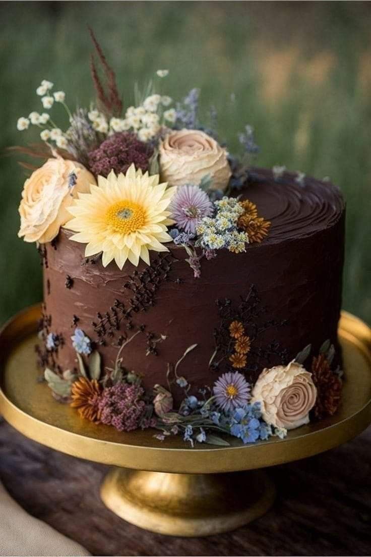 there is a chocolate cake with flowers on the top and sides, sitting on a gold platter