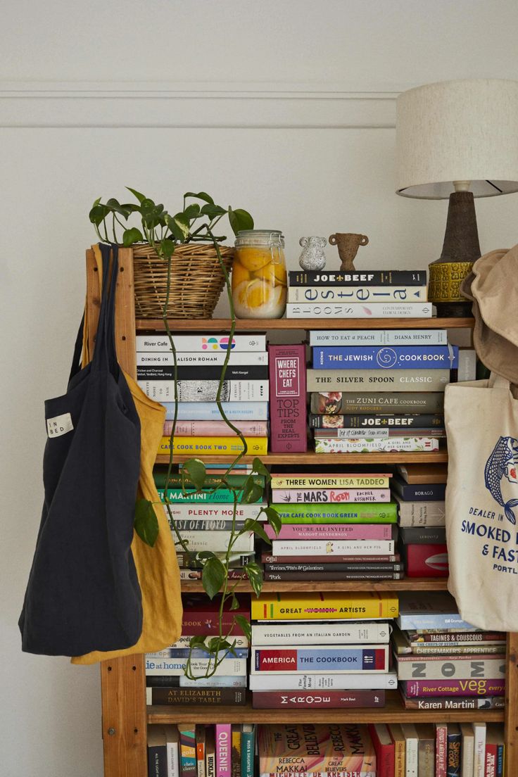 a bookshelf filled with lots of books next to a lamp and a bag