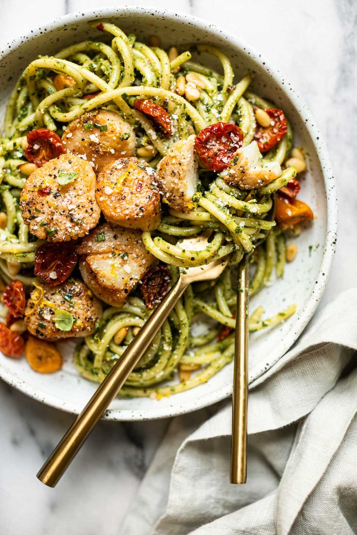 a white bowl filled with pasta, chicken and pesto on top of a marble table