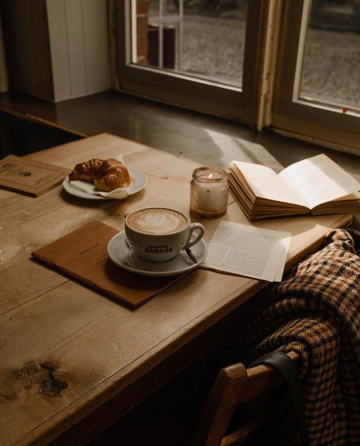 a cup of coffee on a table next to a book and some croissants