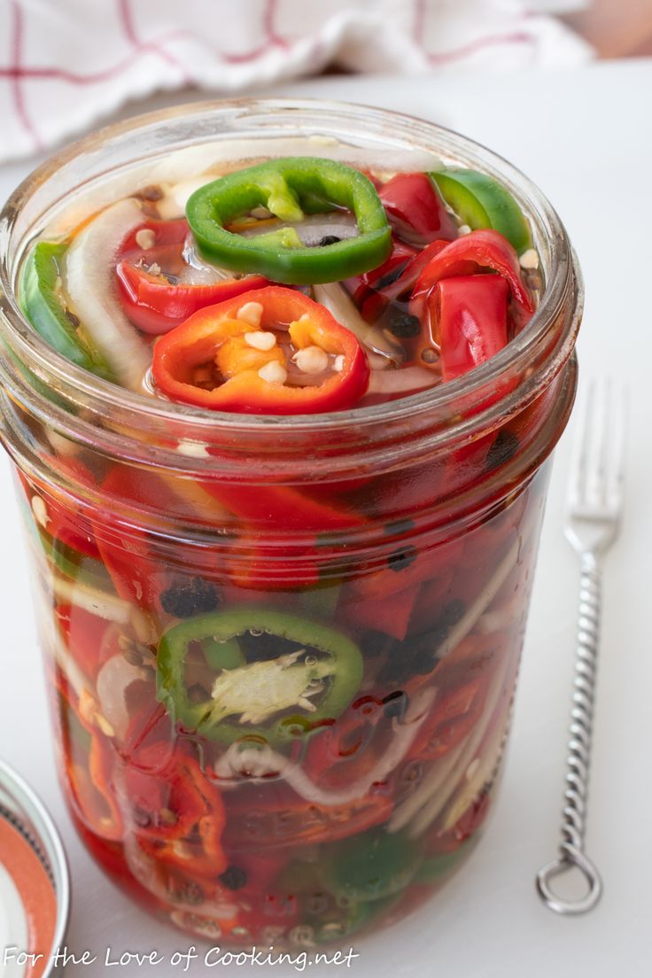 a jar filled with sliced bell peppers on top of a white table next to a fork and knife