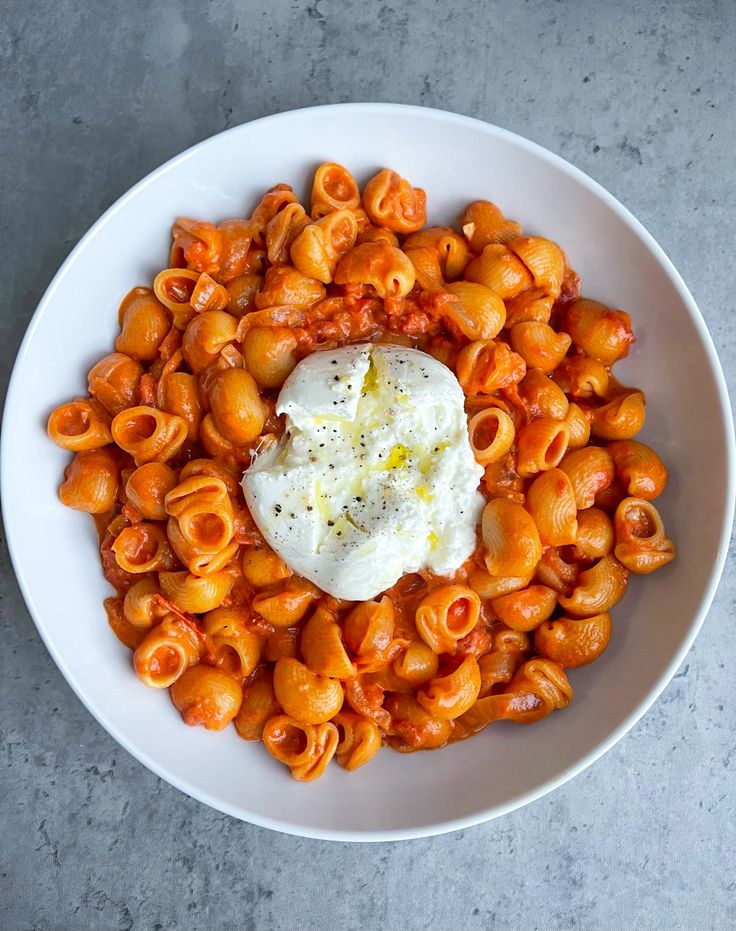 a white bowl filled with pasta and sauce on top of a gray table next to a fork