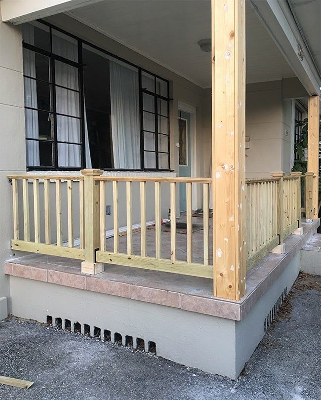 a porch with wooden railings and curtains on the side of a house that is under construction