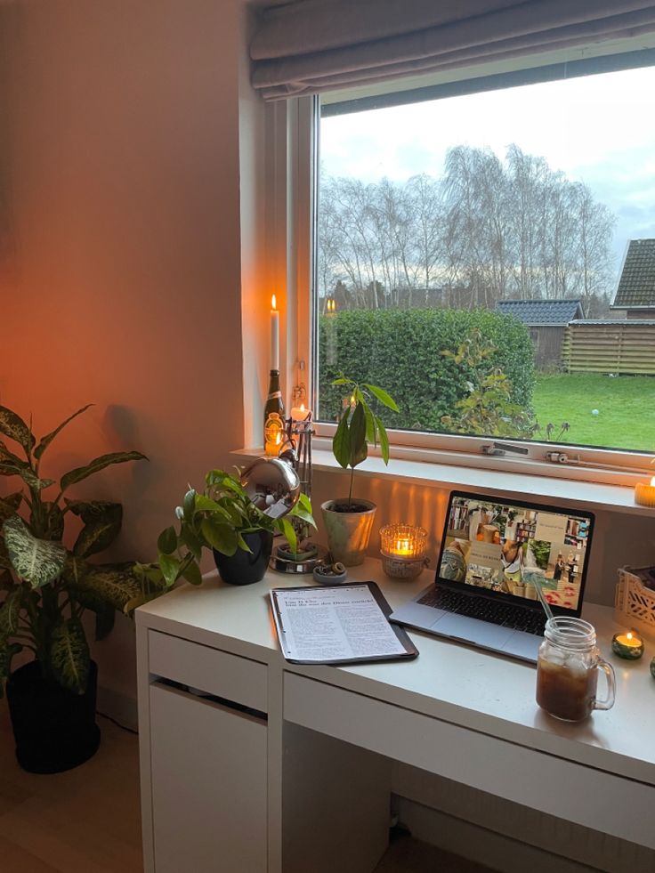 a laptop computer sitting on top of a white desk next to a potted plant