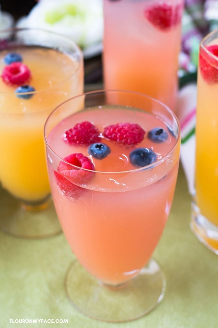 three glasses filled with drinks and garnished with raspberries on a yellow napkin