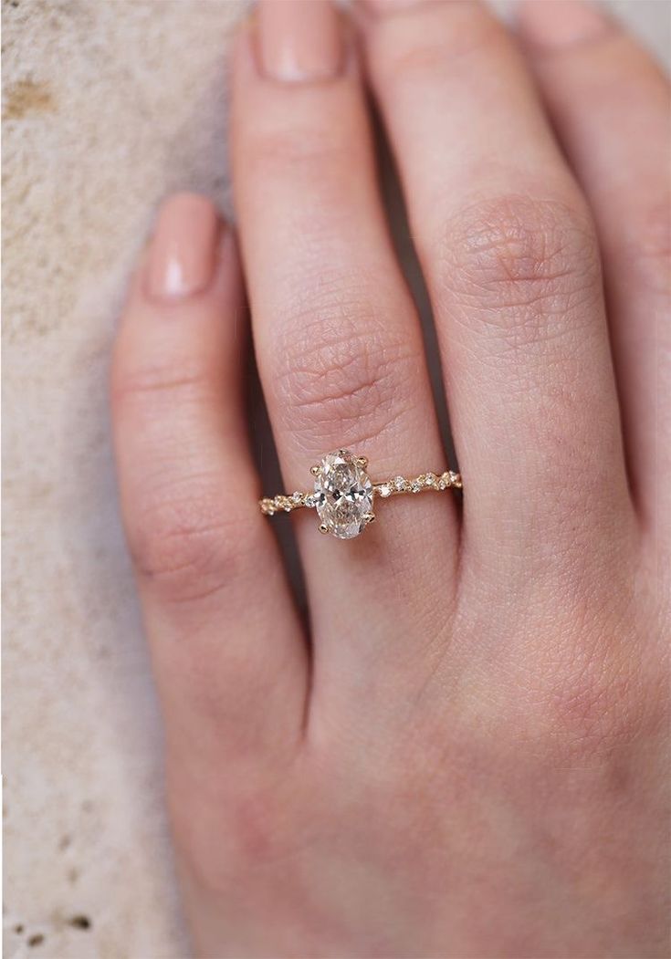 a woman's hand with a diamond ring on top of her finger and the other hand holding an engagement ring