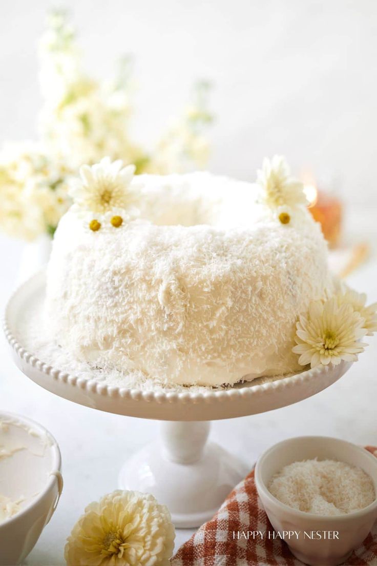 a cake with white frosting and flowers on it sitting on a plate next to bowls