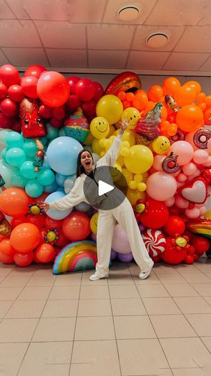 a man standing in front of a large amount of balloons on the floor with his hands up