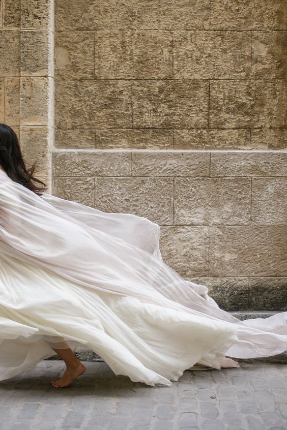 a woman in a white dress is walking down the street with her back to the camera