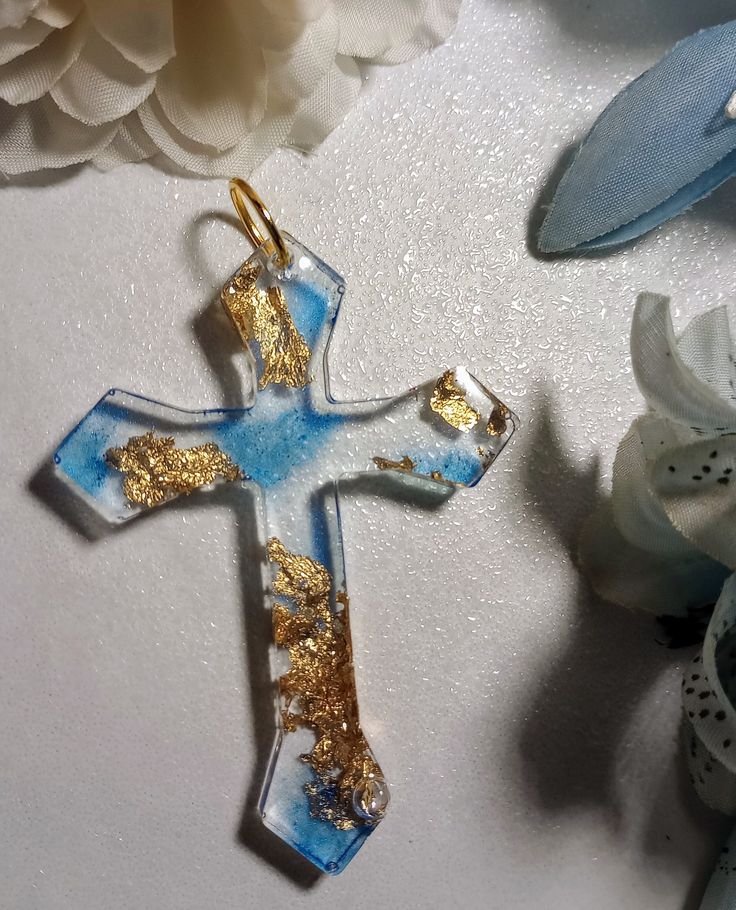 a blue and gold cross is sitting on a white surface next to some flower petals