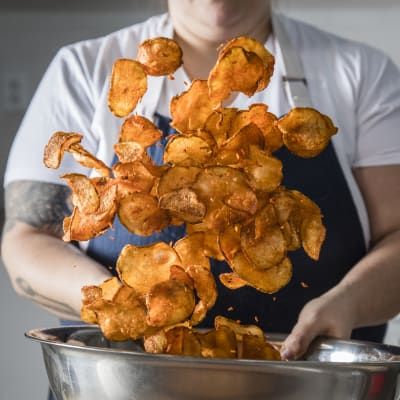 a woman holding a metal bowl filled with fried food