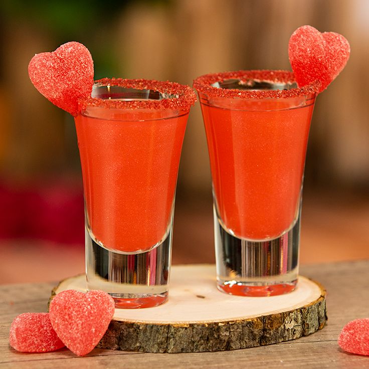 two shot glasses filled with candy hearts on top of a wooden table next to each other