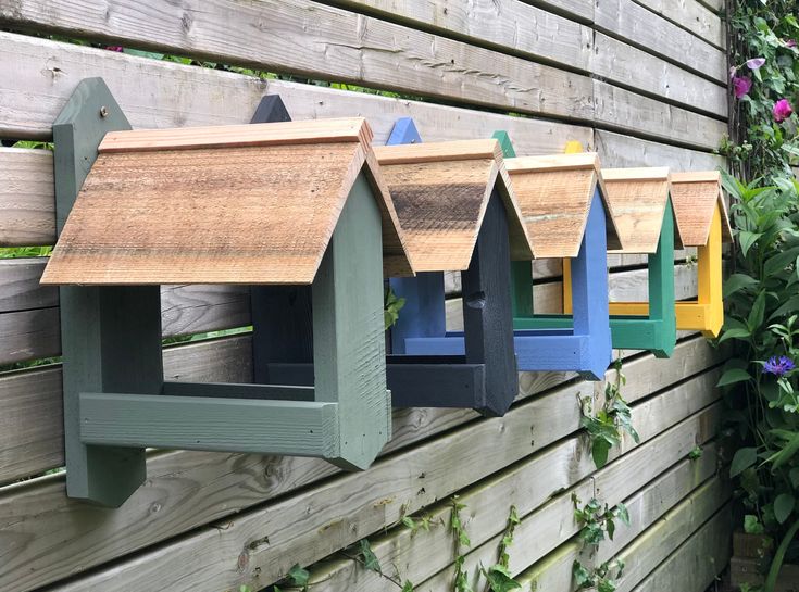 several bird houses are hanging on the side of a fence