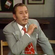 a man in a suit and tie sitting at a table with his hand on his chin