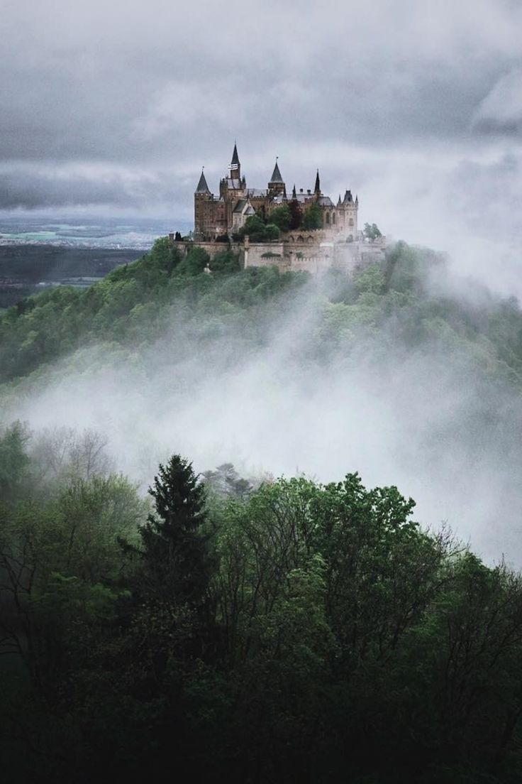 a castle sitting on top of a lush green hillside covered in fog and mists