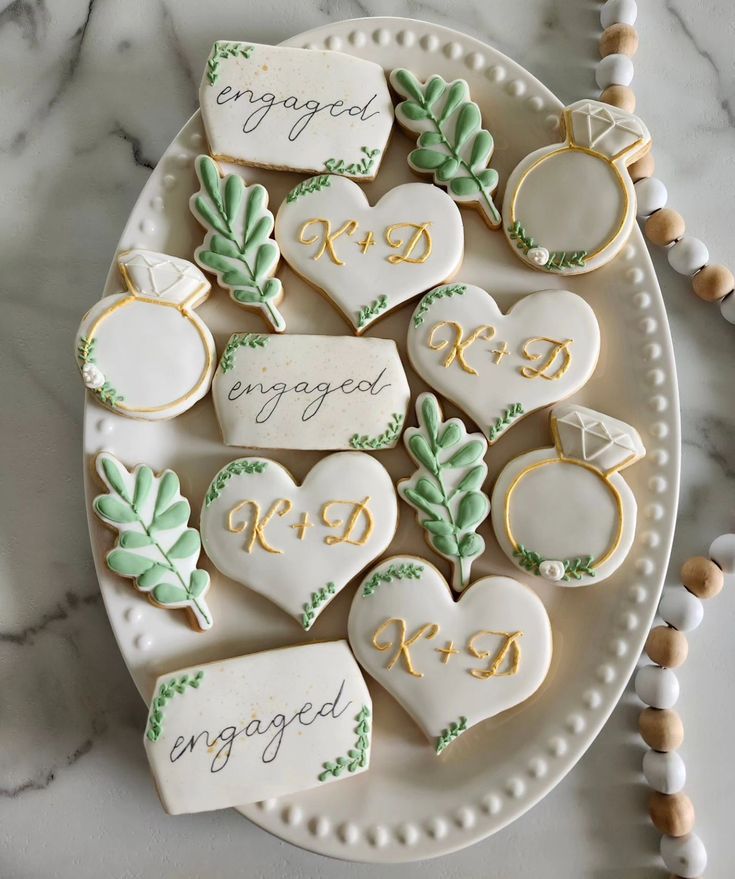 decorated cookies are arranged on a plate with wedding rings and engagement date written on them