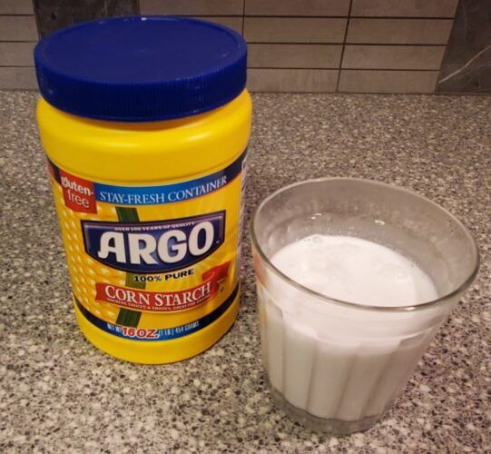 a jar of corn starch next to a glass of milk on a counter top