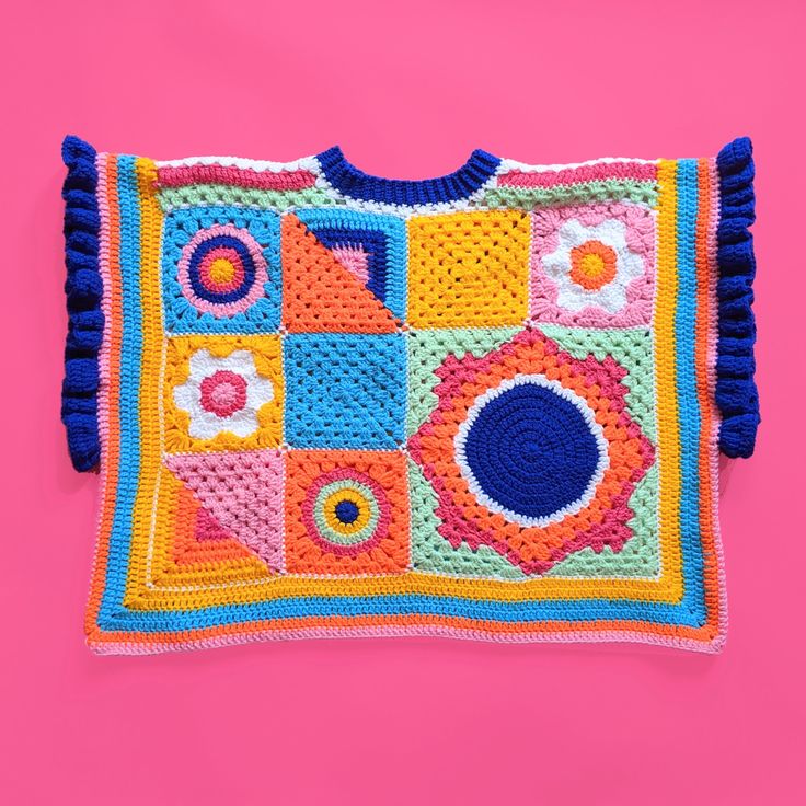 a crocheted square with blue and yellow trim on it sitting on a pink surface