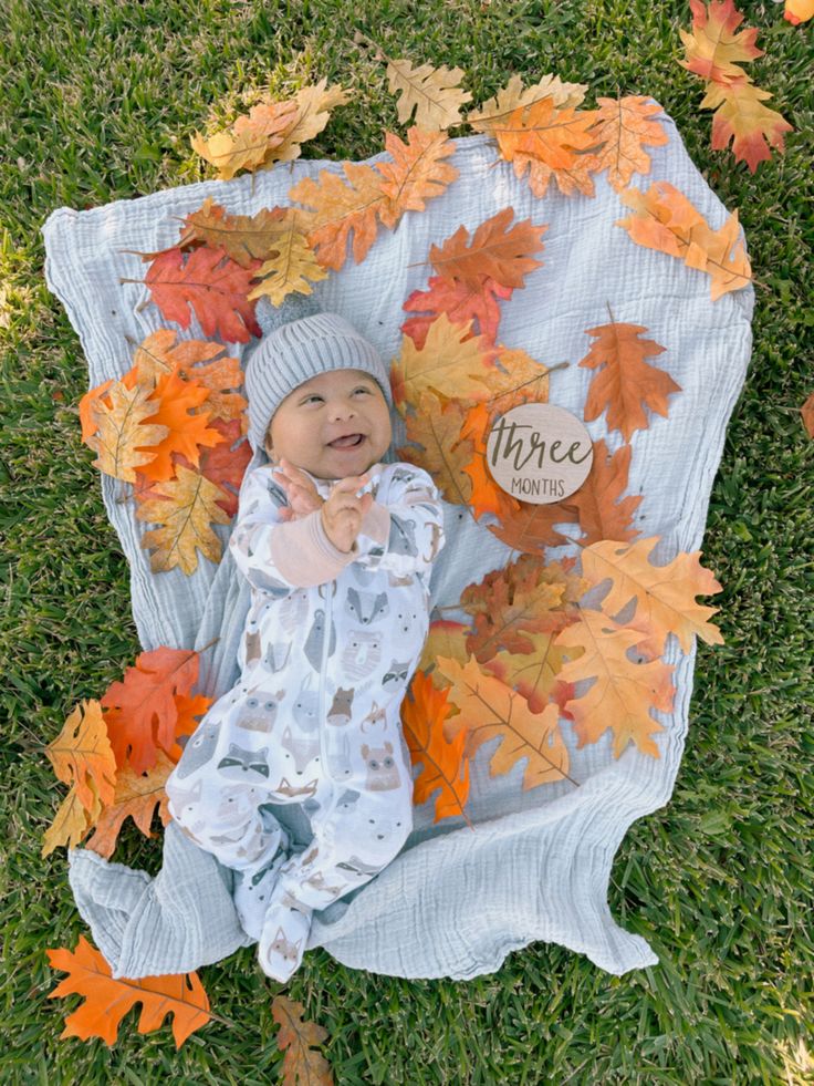 a baby is laying in the grass with autumn leaves on it's back and smiling