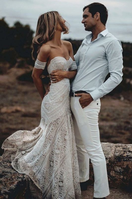 a man and woman standing next to each other in white outfits on the rocky ground