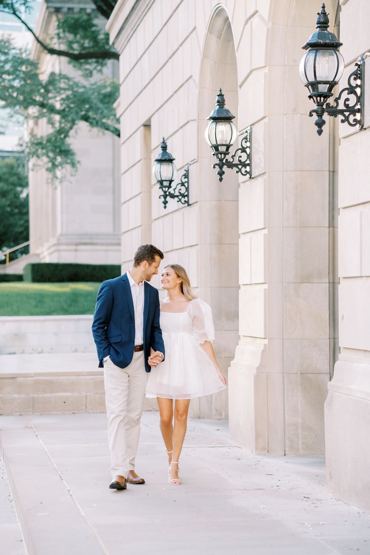 an engaged couple holding hands and walking down the sidewalk