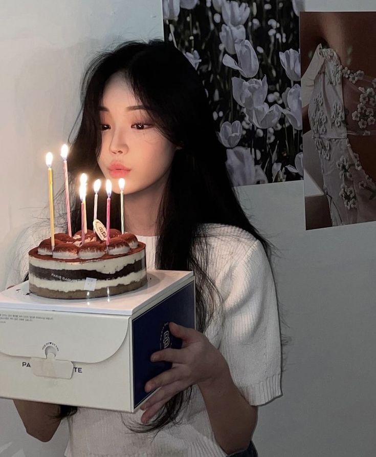 a woman holding a cake with lit candles on it in front of her face,