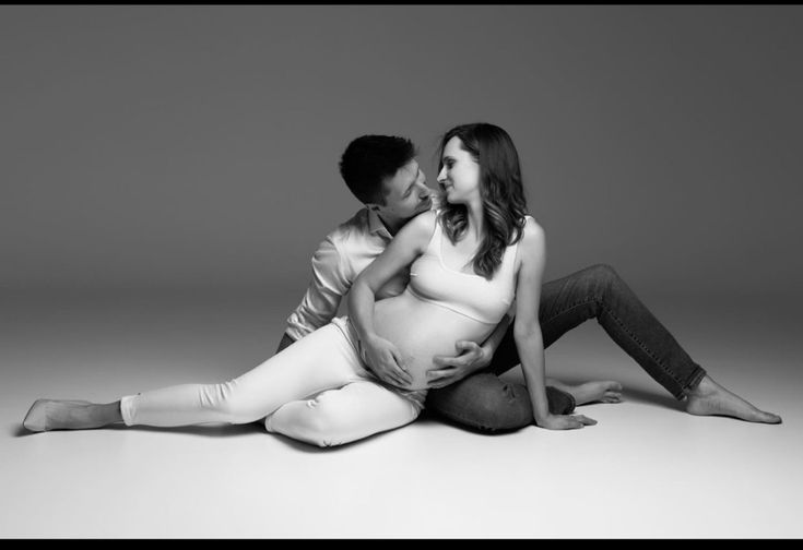 a pregnant woman sitting on the floor next to a man with his arm around her belly