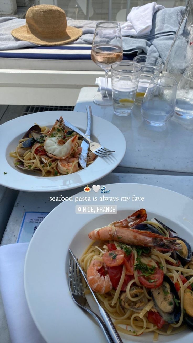 two plates of pasta with shrimp and clams on the table next to wine glasses