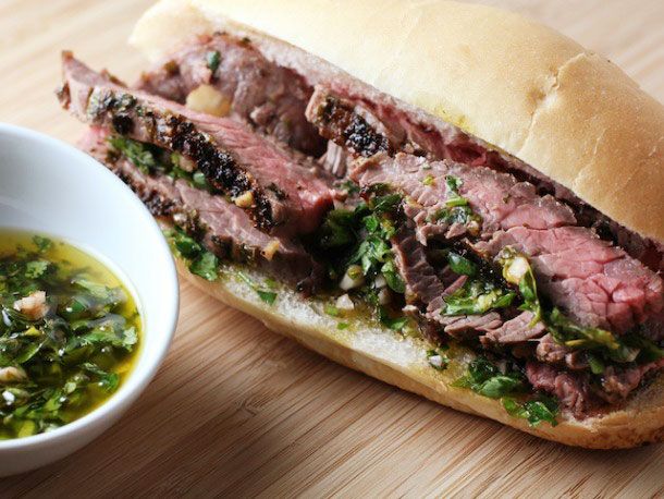 a sandwich with meat and greens next to a bowl of soup on a wooden table