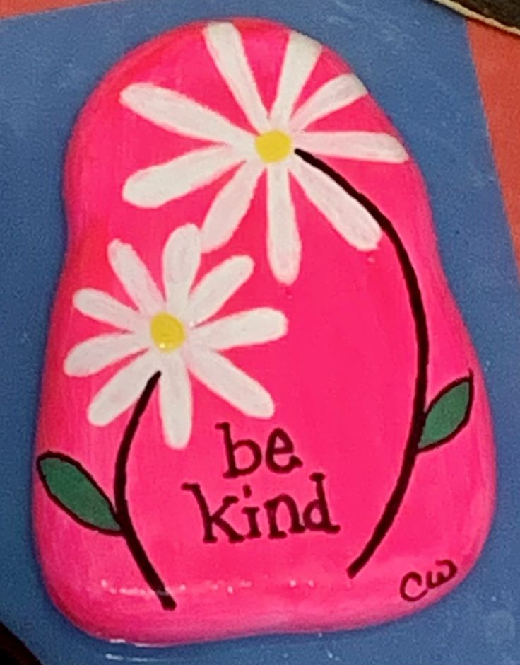 a painted rock that says be kind with daisies on it