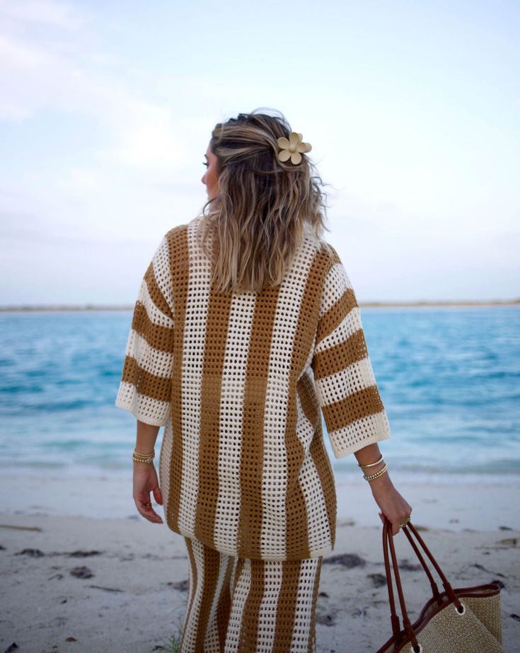 a woman walking on the beach carrying a purse