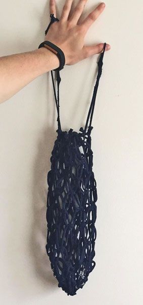 a hand holding onto a string bag hanging on the wall with it's handles