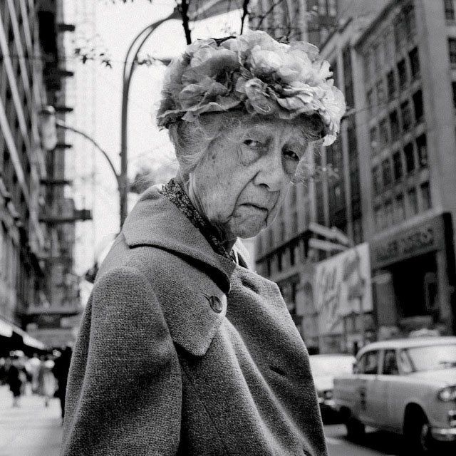 an old woman with flowers on her head walking down the street in new york city