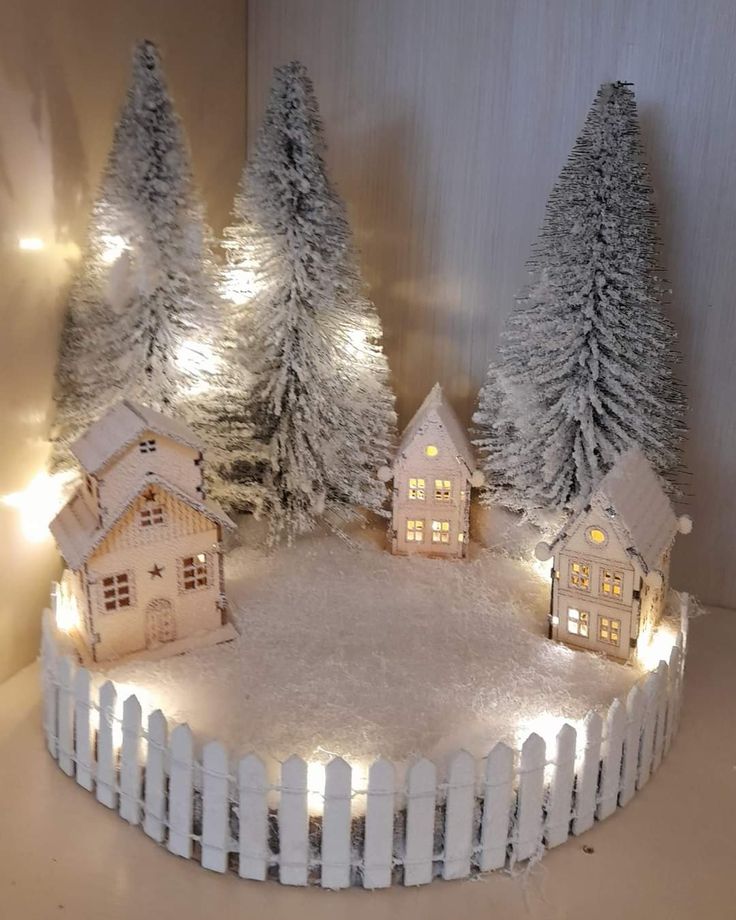 a christmas scene with snow covered trees and small houses on a white fenced in area