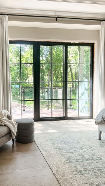 a bedroom with large windows and a white bed in the middle, along with an area rug on the floor