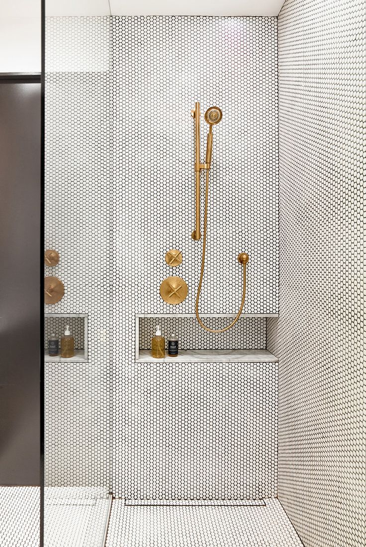 a shower with gold fixtures in a white tiled bathroom