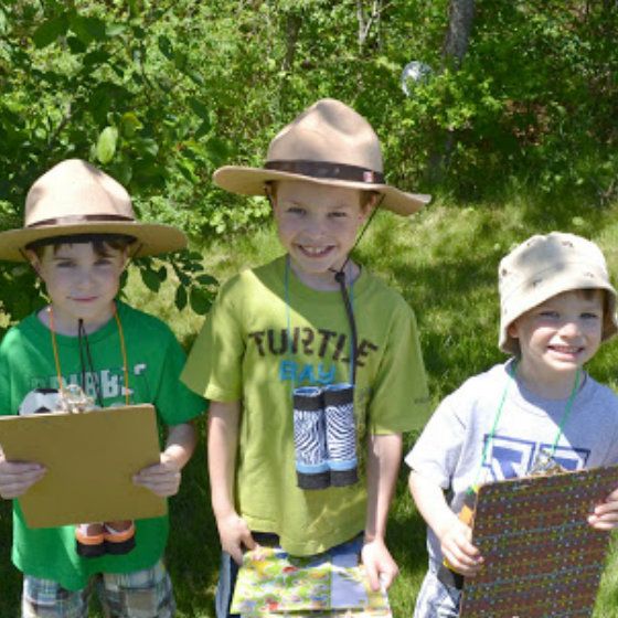 three young boys wearing hats standing next to each other in front of trees and bushes