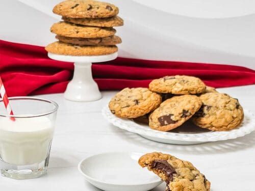 chocolate chip cookies and milk on a white tablecloth with red napkins, glass of milk and plate of cookies