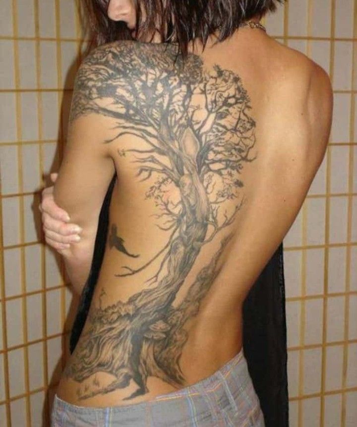 a man with a tree tattoo on his back is standing in front of a tiled wall