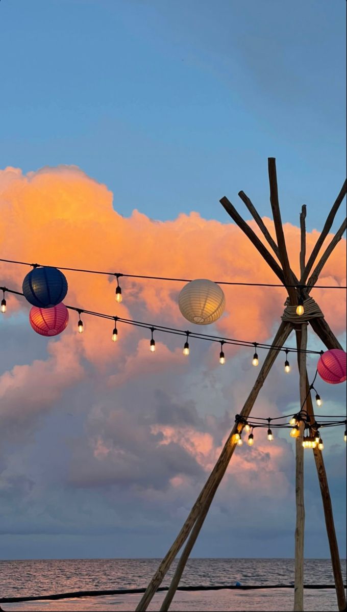 some lights are hanging from a line over the water and clouds in the sky above