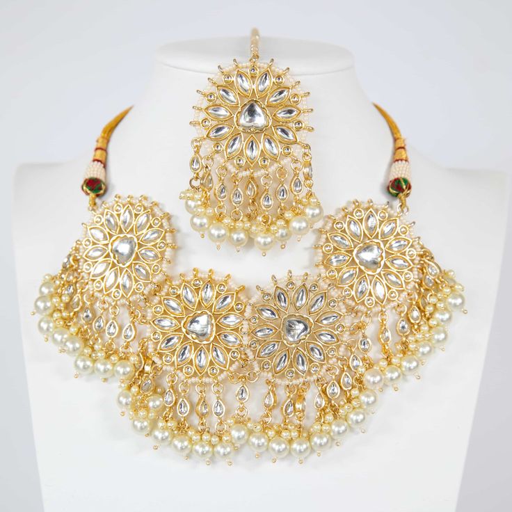 Unveil your elegance this festive season with our Deepika Kundan Choker Set—a stunning embodiment of Indian tradition infused with a modern edge. This magnificent set, meticulously crafted by skilled artisans, is an ode to the timeless beauty of kundan jewelry. The choker, embellished with intricate kundan work and delicate pearls, rests gracefully on a base of gleaming gold plating, making it an ideal companion for sarees, lehengas, or any festive attire. Paired with matching earrings and a str Kundan Choker Hand Set For Diwali, Festive Kundan Choker With Hand Set Details, Festive Kundan Hand Set Choker, Festive Kundan Set With Intricate Design, Gold Kundan Choker With Gota Work, Kundan Choker With Intricate Design For Festive Occasions, Kundan Necklaces With Gota Work For Celebration, Festive Kundan Choker With Intricate Design, Kundan Jewelry Sets With Cutdana For Celebration