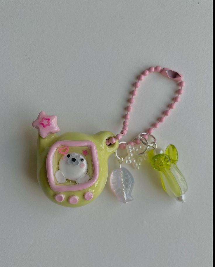 a small green and pink cell phone charm with a white cat in a car on it