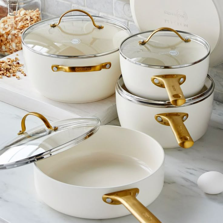 white pots and pans with gold handles sitting on a marble countertop next to an egg