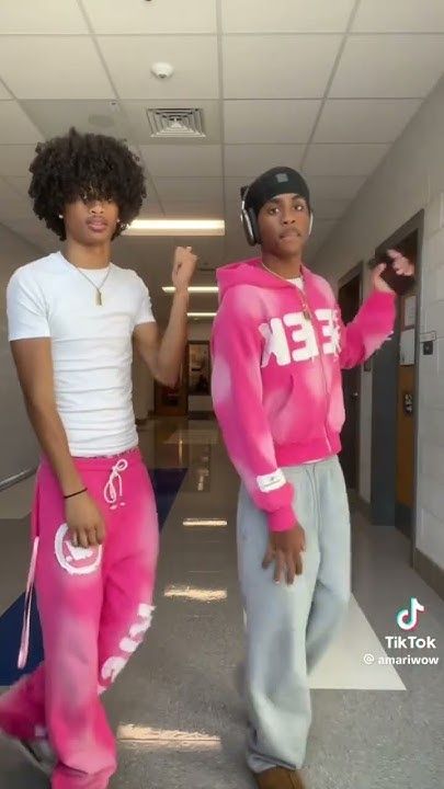 two young men dressed in pink and white outfits standing next to each other on a hallway