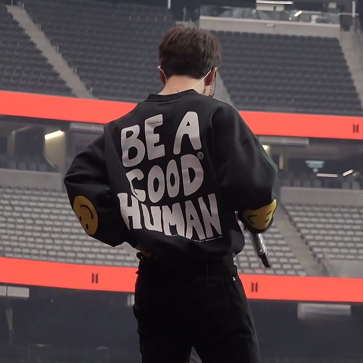 a man standing in front of an empty bleachers wearing a jacket that says be a good human